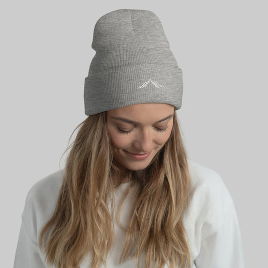Woman wearing a grey beanie with a skoggl logo against a light gray background