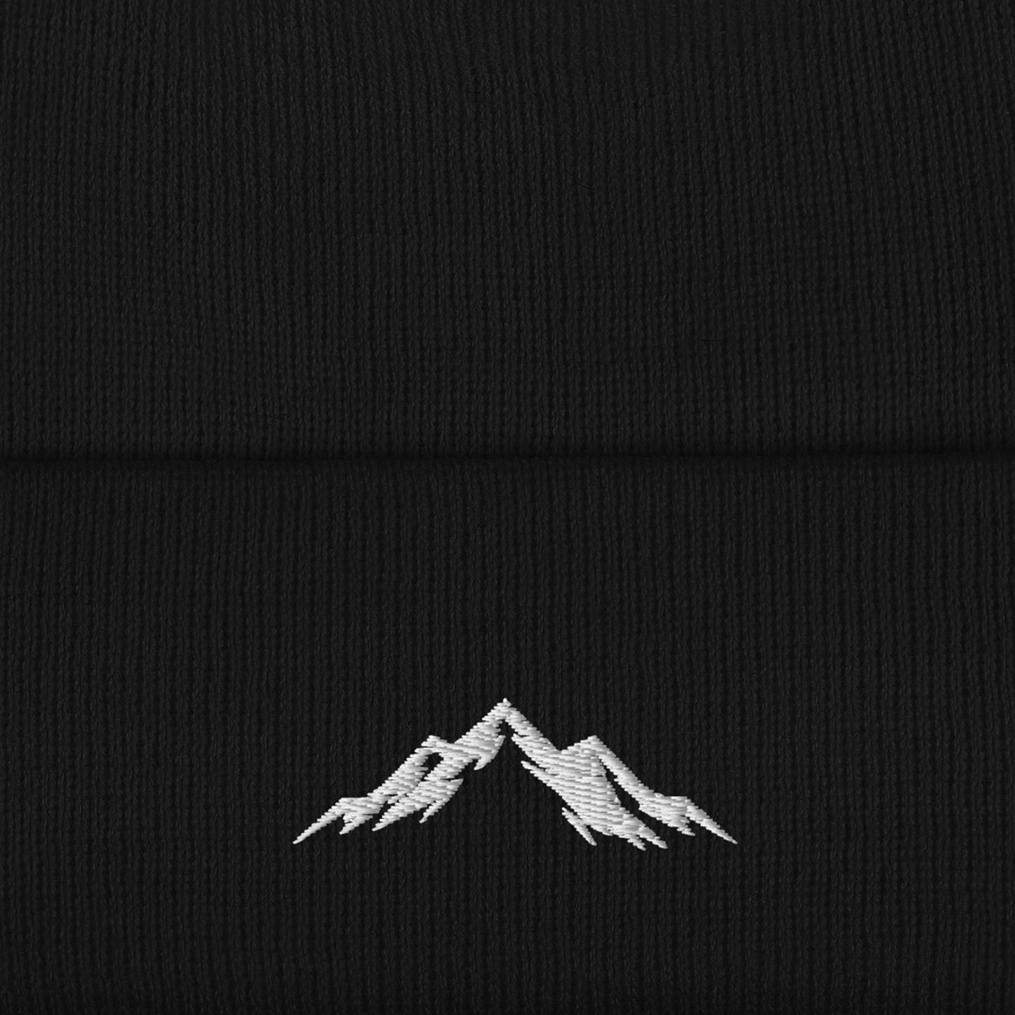 close-up of a white embroidered mountain Skoggl logo on a black beanie