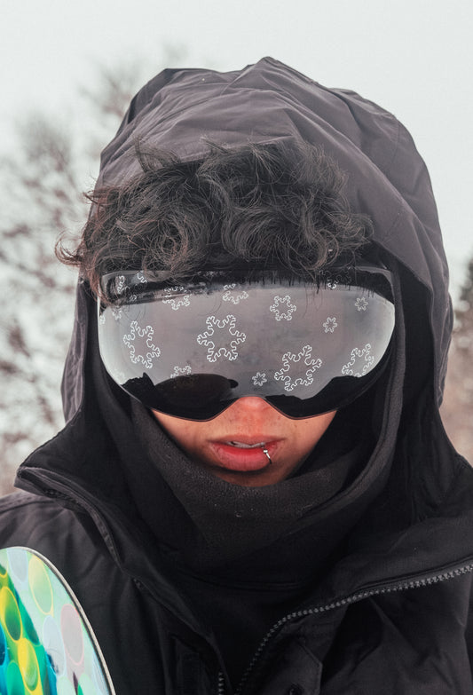 Close-up of a magnetic ski and snowboard goggle lens with a snowflake design in silver, set in a sleek black frame and strap for a modern, minimalist look. Highlights the magnetic lens system for quick, easy swaps, offering versatile performance and style on the slopes.