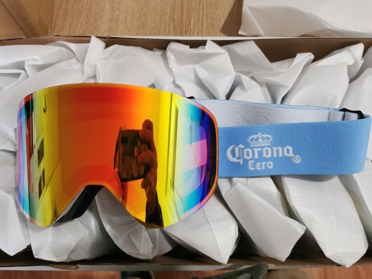 Skoggl custom Corona Cero branded snowboard goggles for the Milano Cortina Olympic Winter Games, showcasing a vibrant orange-to-blue gradient mirror lens and a light blue embroidered logo strap.