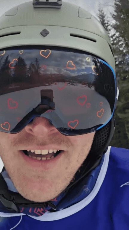 Paralympian Mathew Hamilton wearing Skoggl custom ski goggles with a red heart-patterned reflective lens and a matte grey helmet on a snowy slope.