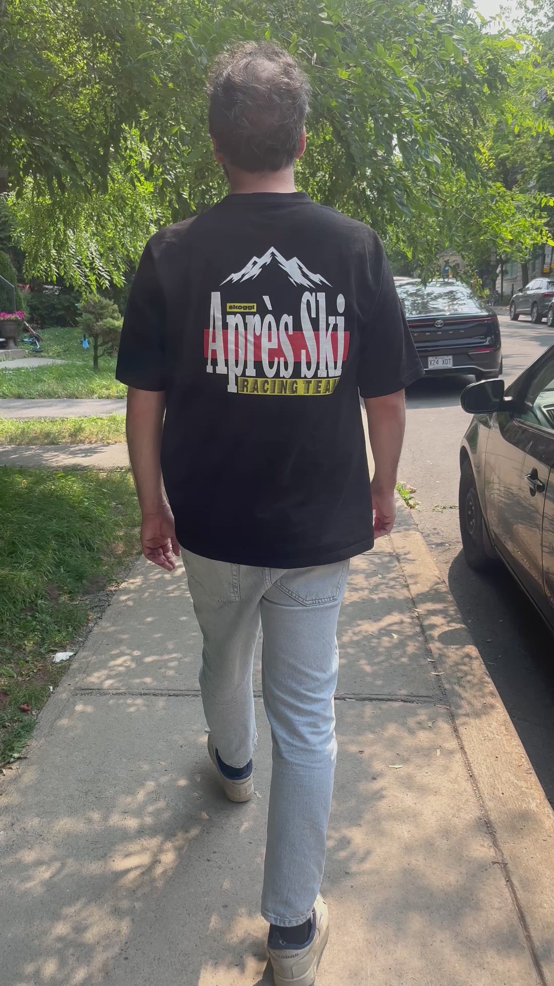 Model walking down a city road wearing the black ovrersized Skoggl Après Ski Team Tee on the back of the tee.