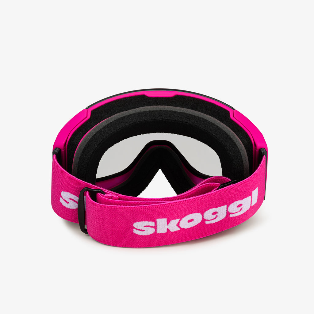 Pink ski goggles with a wide pink strap featuring the word 'Skoggl', shown from the back. Clear lenses are visible through the frame, paired with black cushioning for comfort and a secure fit. Perfect for customizable, stylish ski and snowboard gear designed for performance on the slopes.