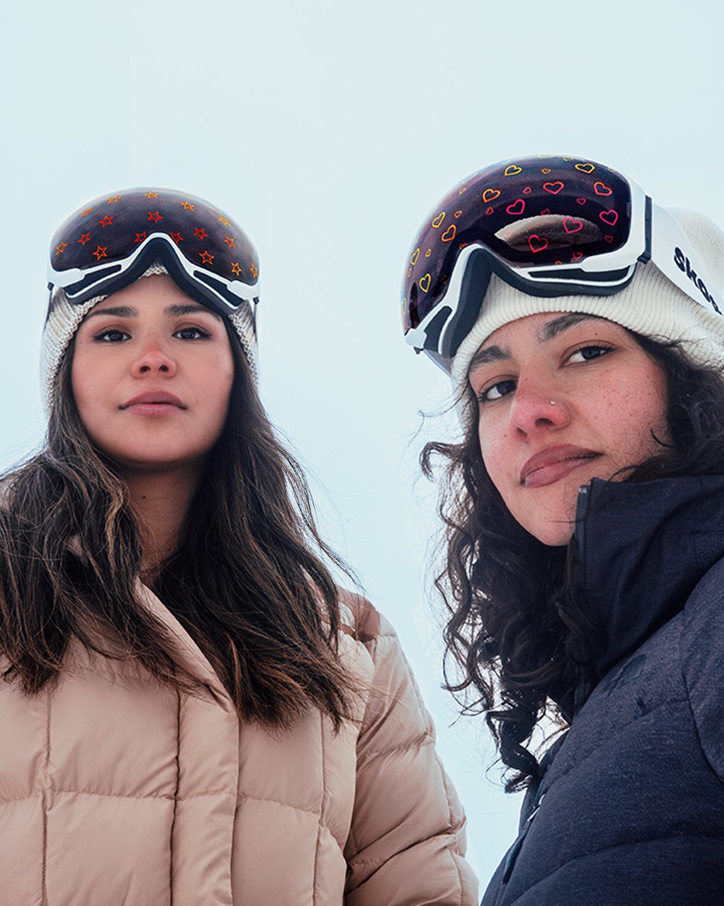 Two women wearing Skoggl ski goggles with unique star and heart lens designs looking at the camera.
