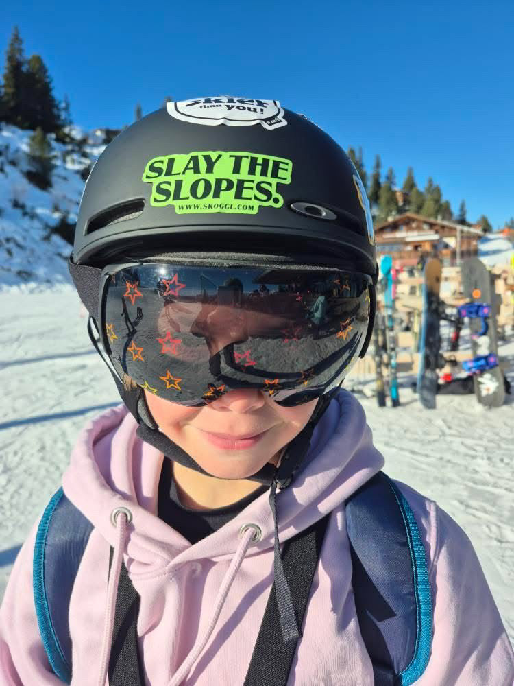 GB Freestyle Skiing Champion Hatti Wilson wearing Skoggl children's ski goggles with orange star-patterned magnetic lenses and a black 'Slay the Slopes' sticker from Skoggl on her helmet.