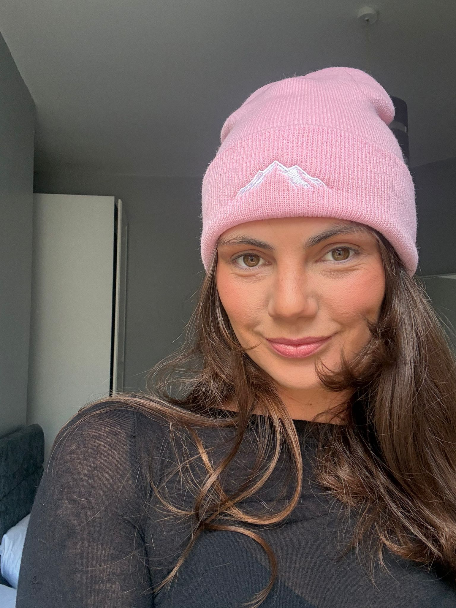 Woman wearing a pink skoggl beanie with mountain logo indoors.