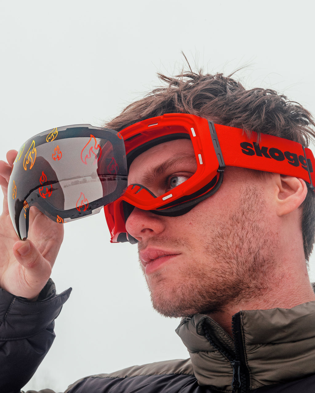 Man wearing red Skoggl ski goggles with interchangeable magnetic flame-pattern lens on snowy mountain