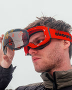 Man wearing red Skoggl ski goggles with interchangeable magnetic flame-pattern lens on snowy mountain