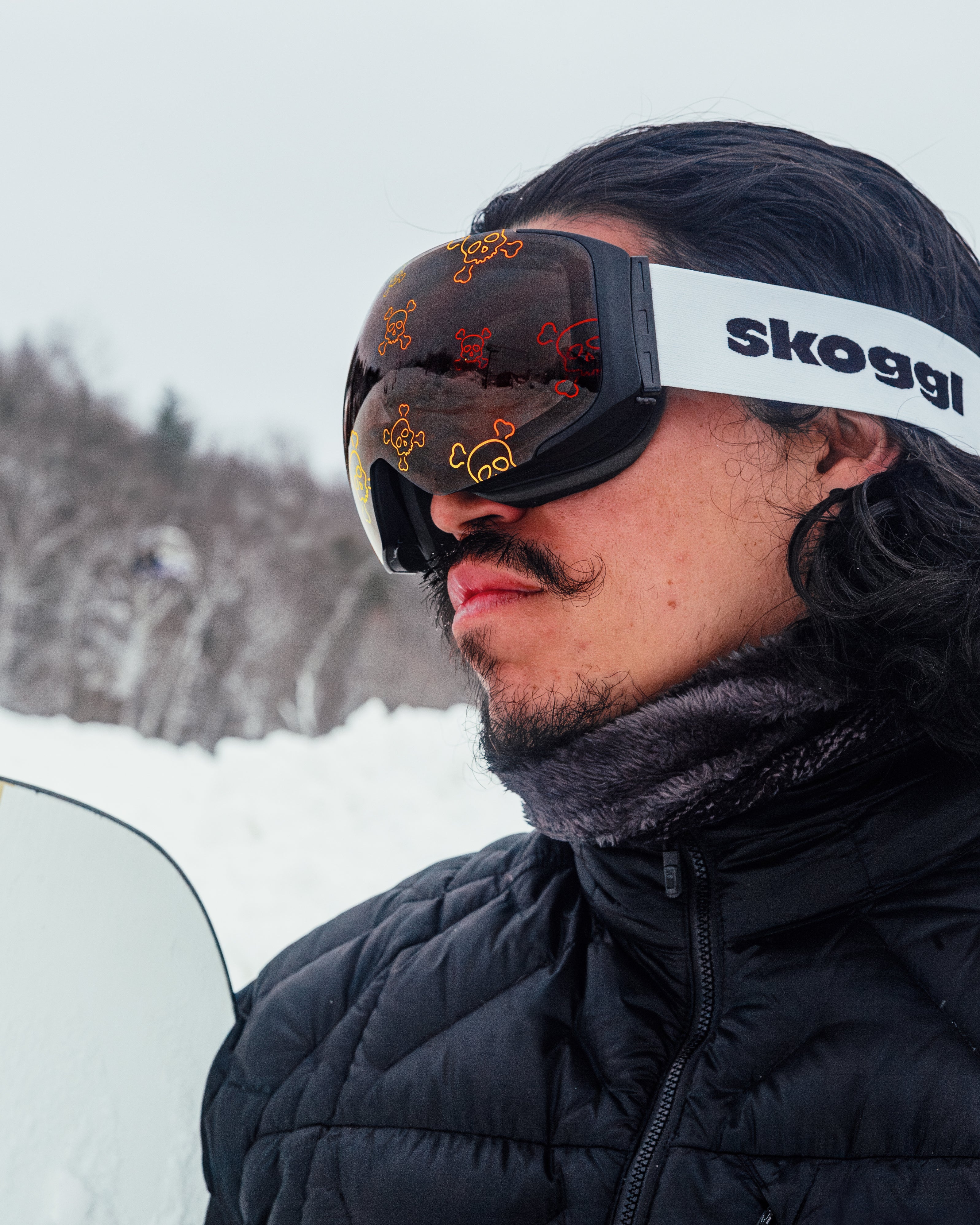 Male skier wearing black and white Skoggl ski goggles with interchangeable magnetic skull design pattern lens on snowy mountain