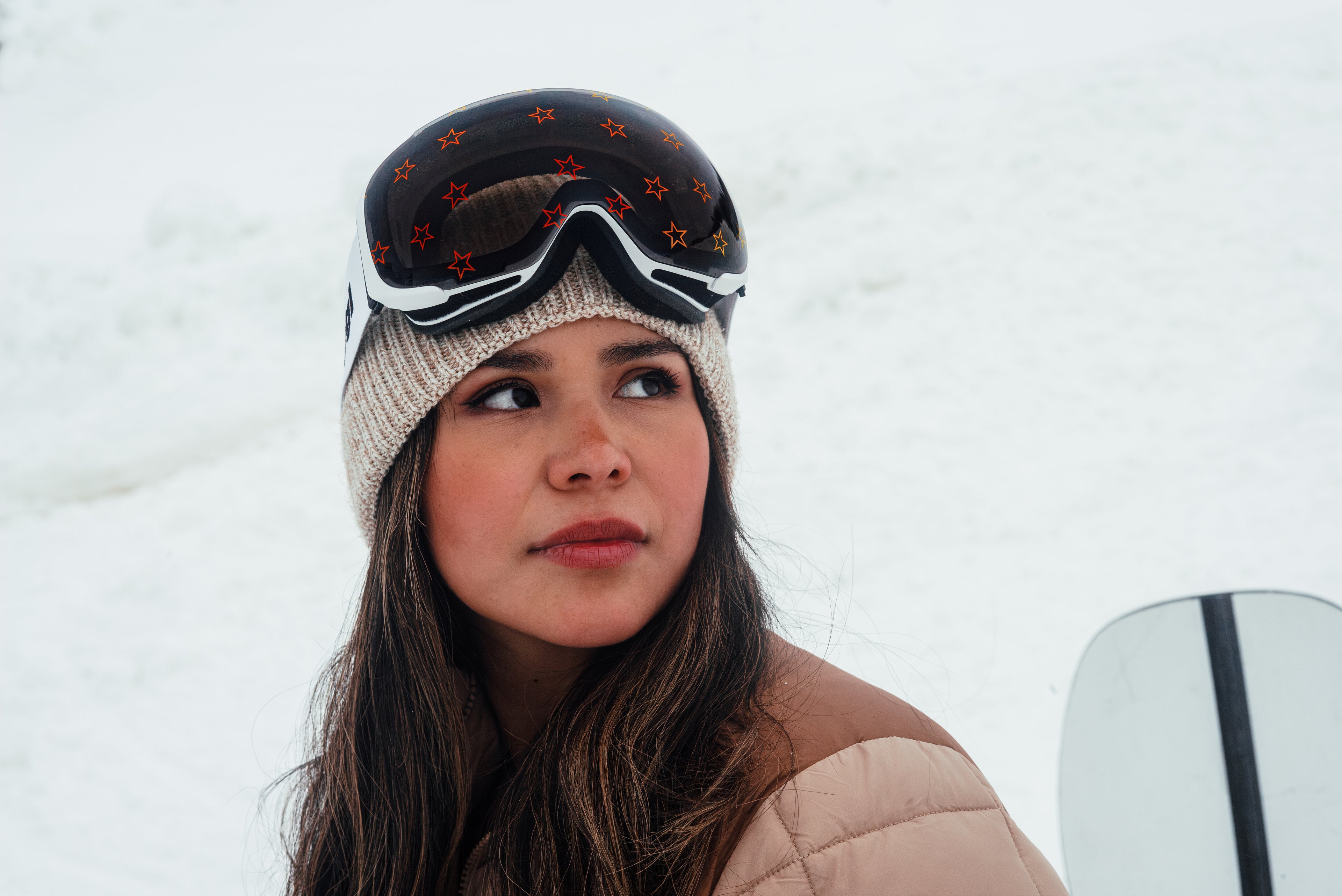 Model wearing Skoggl ski goggles with a white frame and Star Struck lens featuring star designs, set against a snowy backdrop.