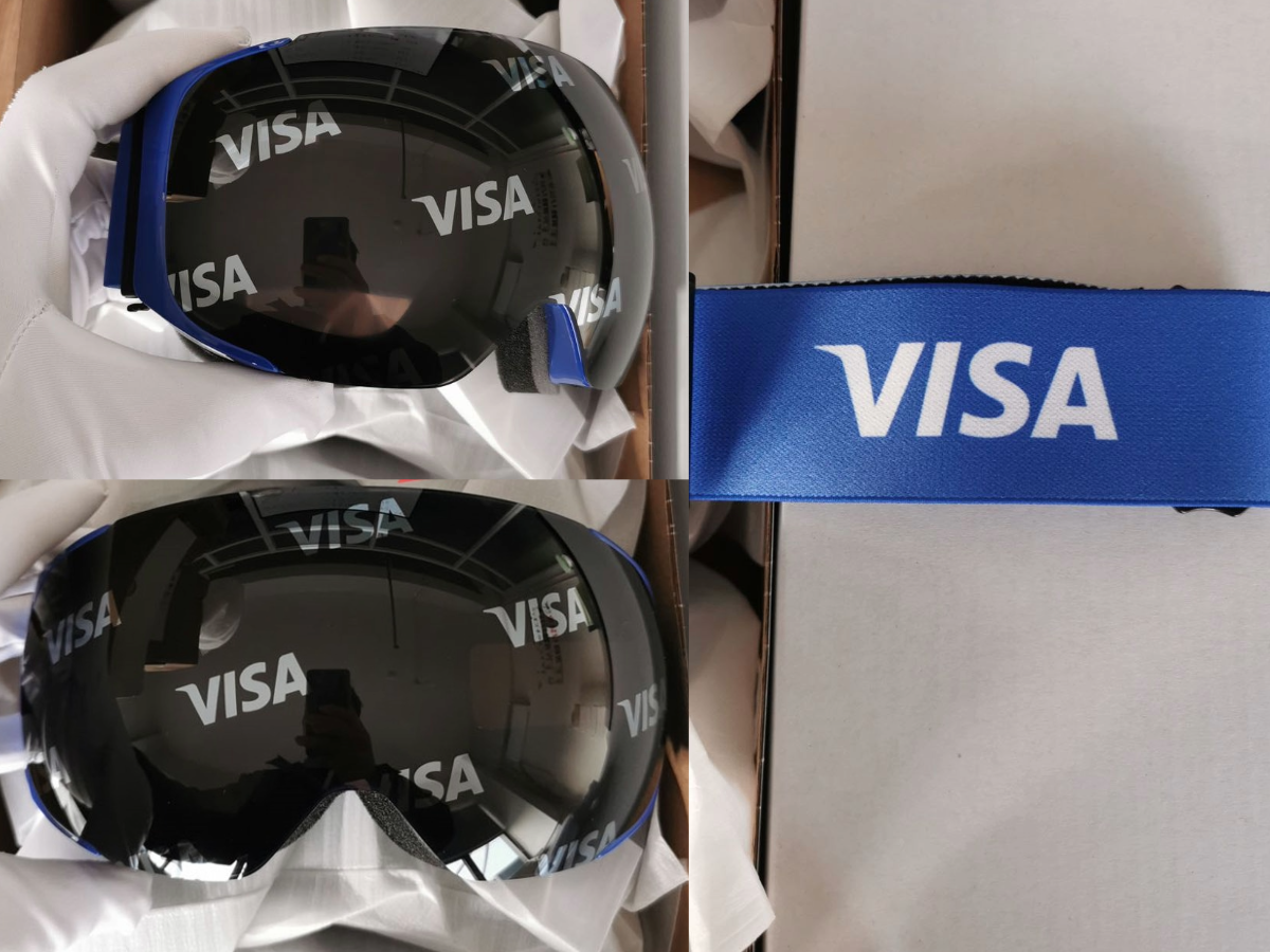 Custom branded Visa ski goggles by Skoggl for the Milano Cortina 2026 Winter Olympics, featuring a black mirror lens with a repeating Visa logo pattern and a matching blue logo strap.